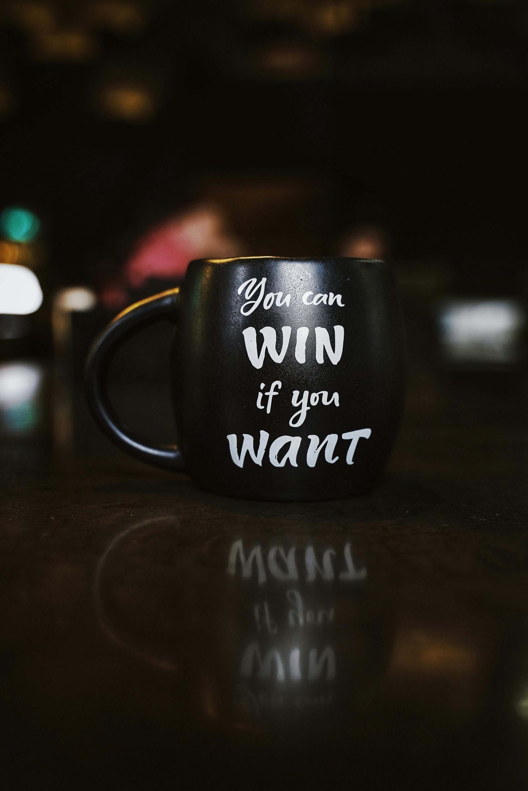 Black mug with inspirational quote 'You can win if you want' reflected on a dark surface, creating a motivational ambiance.