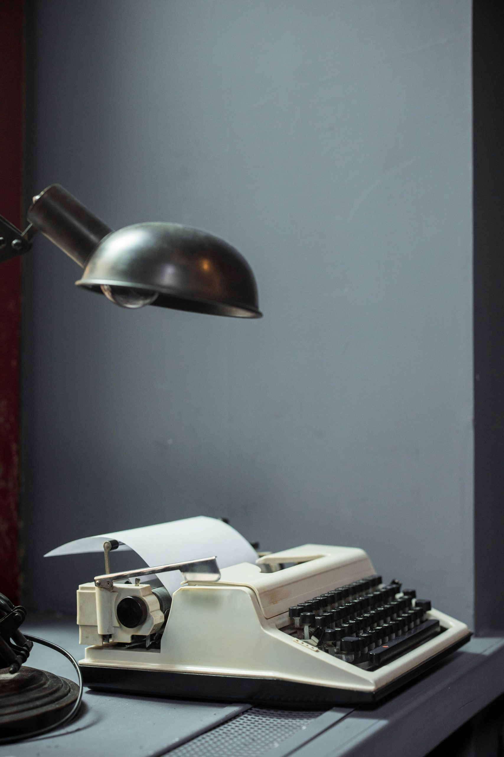 A classic typewriter and desk lamp on a desk in a room with gray walls. Vintage office setup.